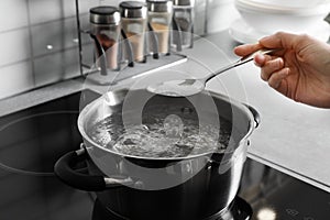 Woman salting boiling water in pot on stove