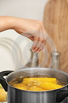 Woman salting water with corn cobs in stewpot