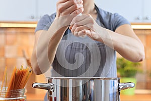 Woman salting water in a pot on a stove in the kitchen