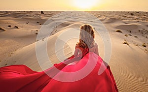 Woman in sands dunes of desert at sunset