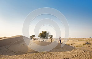 Woman in sands dunes of desert at sunset