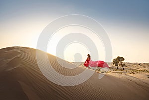 Woman in sands dunes of desert at sunset