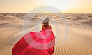 Woman in sands dunes of desert at sunset