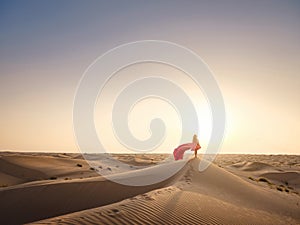 Woman in sands dunes of desert at sunset