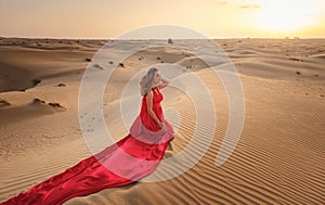 Woman in sands dunes of desert at sunset