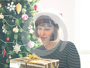 Woman in santa cap holding wrapped gift, christmas tree behind