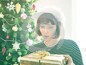 Woman in santa cap holding wrapped gift, christmas tree behind