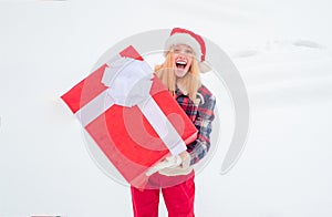 Woman in Santa Claus dress giving you big red gift over white snow background. Woman present red gift box with ribbon