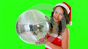 Woman in Santa dress keep disco ball. Green background.