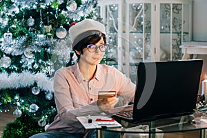 Woman in Santa hat holding credit card and have shopping online on Christmas sales with festive Christmas tree