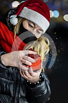 A woman in a Santa hat opens a festive red gift box. Christmas holidays