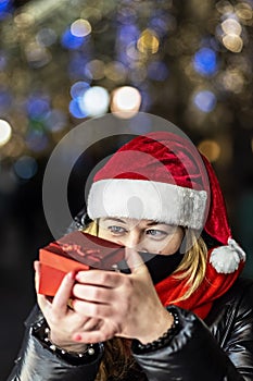 A woman in a Santa hat opens a festive red gift box. Christmas holidays