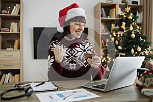 Woman in Santa hat raising fist while looking at laptop with credit card in hand