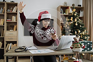 Woman in Santa hat raising palm hand while looking at laptop with credit card.