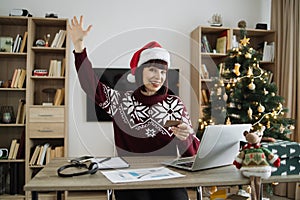 Woman in Santa hat raising palm hand while looking at laptop with credit card.