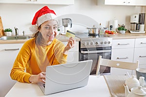 Woman in Santa hat shopping online and paying with gold credit card. Young girl with laptop buying Christmas gift present on