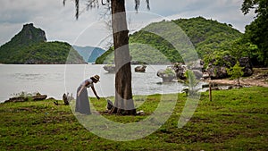 Woman in sarong and white fedora leaning down and feeding dusky Monkey