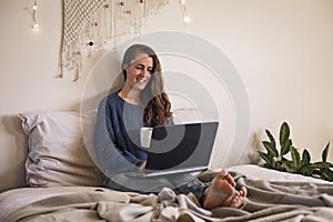 Woman sat in bed using laptop computer
