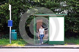Woman sat at a bus stop next to blank billboard