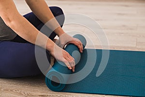 Woman sat cross legged in yoga studio rolling her mat