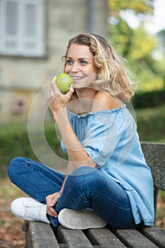 woman sat on outdoor bench eating apple