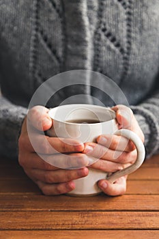 Woman sat at table with mug of tea wearing cozy gray cardigan