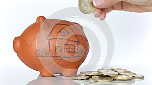 Woman saving money into a traditional clay piggy bank for a house