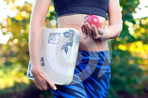 Woman with scale and red apple outdoor. Slimming, diet and healthy lifestyles concept