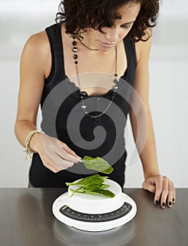 Woman, scale and spinach in kitchen for food, diet or eating disorder with leaves for meal plan. Girl, mental health and