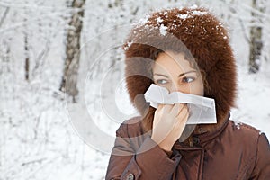 Woman with scarf blowing nose in wood in winter