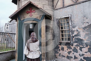 A woman in a scarf and old clothes at the entrance to the old European Church. Retro style on Halloween, 18-19th century