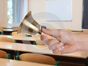 Woman with school bell in empty classroom, closeup