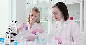Woman scientist gives glass with reagent to blonde assistant