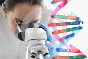 Woman scientist looking through microscope near dna molecule mockup in lab