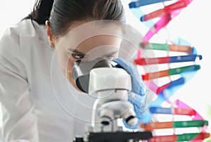 Woman scientist looking through microscope near dna molecule mockup in lab
