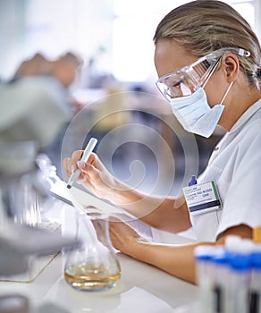 Woman, scientist and writing with mask for research, checklist or test results from experiment at laboratory. Female photo