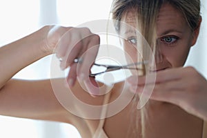 A woman scissors cuts her own hair, close-up