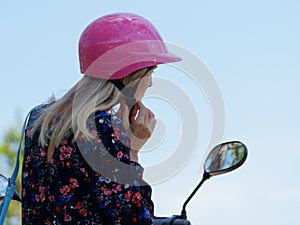 Woman on scooter tightens pink helmet.