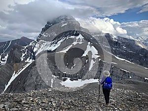 Woman  scrambling up scree  to snowcapped peak in Canadian Rockies.