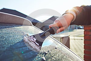 A woman scrapes frost off the front window of her car