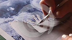 A woman scrapes a printed photo with a cutter