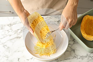 Woman scraping flesh of cooked spaghetti squash with fork