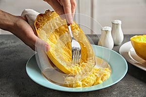Woman scraping flesh of cooked spaghetti squash with fork on table