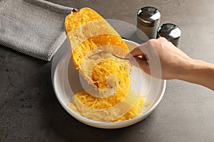 Woman scraping flesh of cooked spaghetti squash with fork at table
