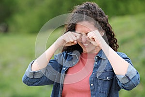 Woman scratching itchy eyes in a green park