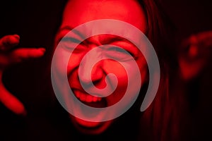 Woman screaming close-up to camera in red neon light, furious face, hysterics