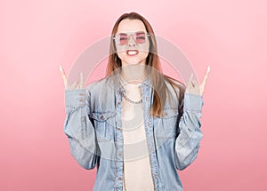 woman screaming with crazy expression making rock symbol with raised hands in pink glasses. Heavy concept