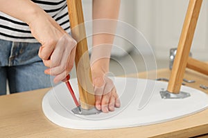 Woman with screwdriver assembling stool at table indoors, closeup