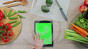 Woman scrolls through recipes on her tablet in the kitchen. Application for cooking. Healthy food concept.