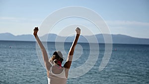 Woman by the sea enjoying life as she lifts her arms high up in celebration